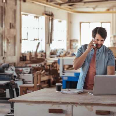 Woodworker using a phone and a laptop in his workshop