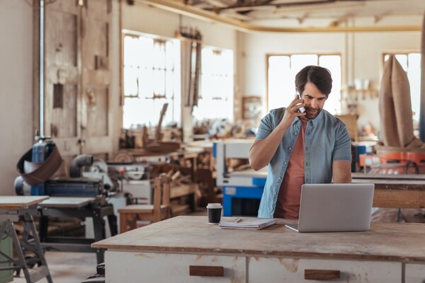 Woodworker using a phone and a laptop in his workshop