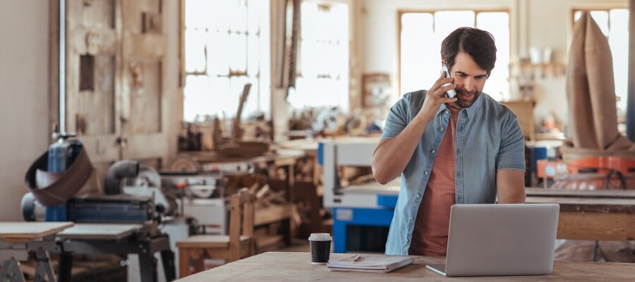 Woodworker using a phone and a laptop in his workshop